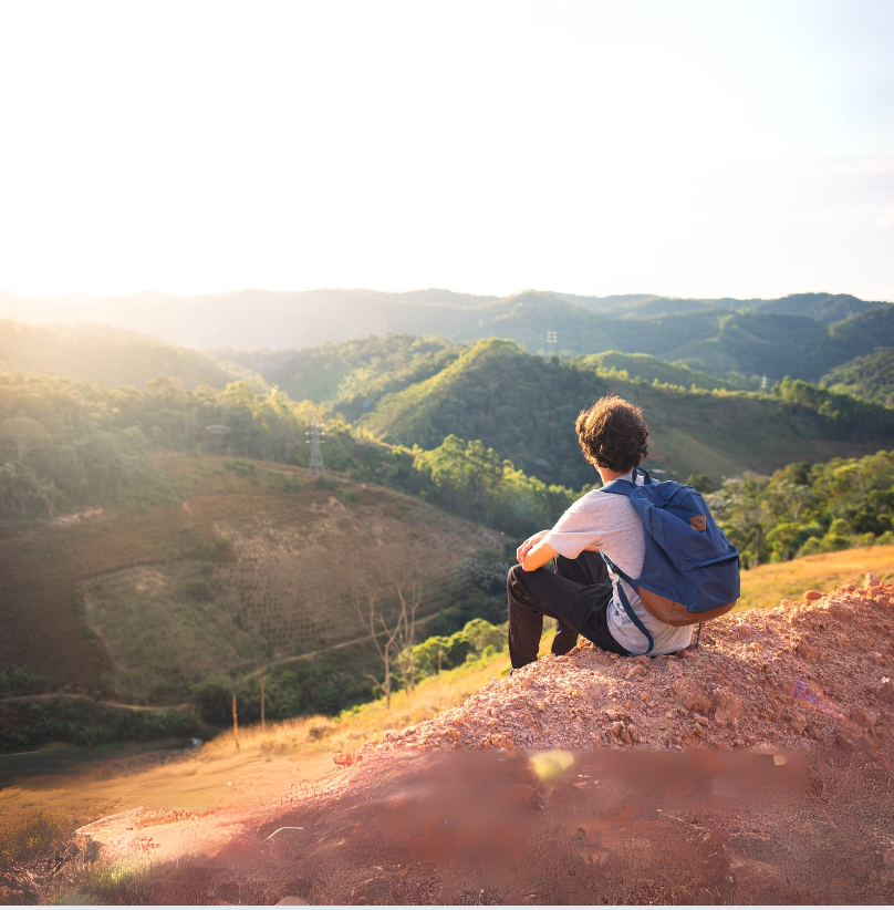 Man sits on mountain overlooking green forest to improve wellness